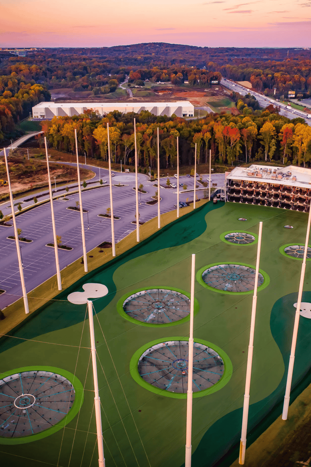 Vintage driving range with green turf and golf ball collectors, surrounded by parking and scenic fall foliage.