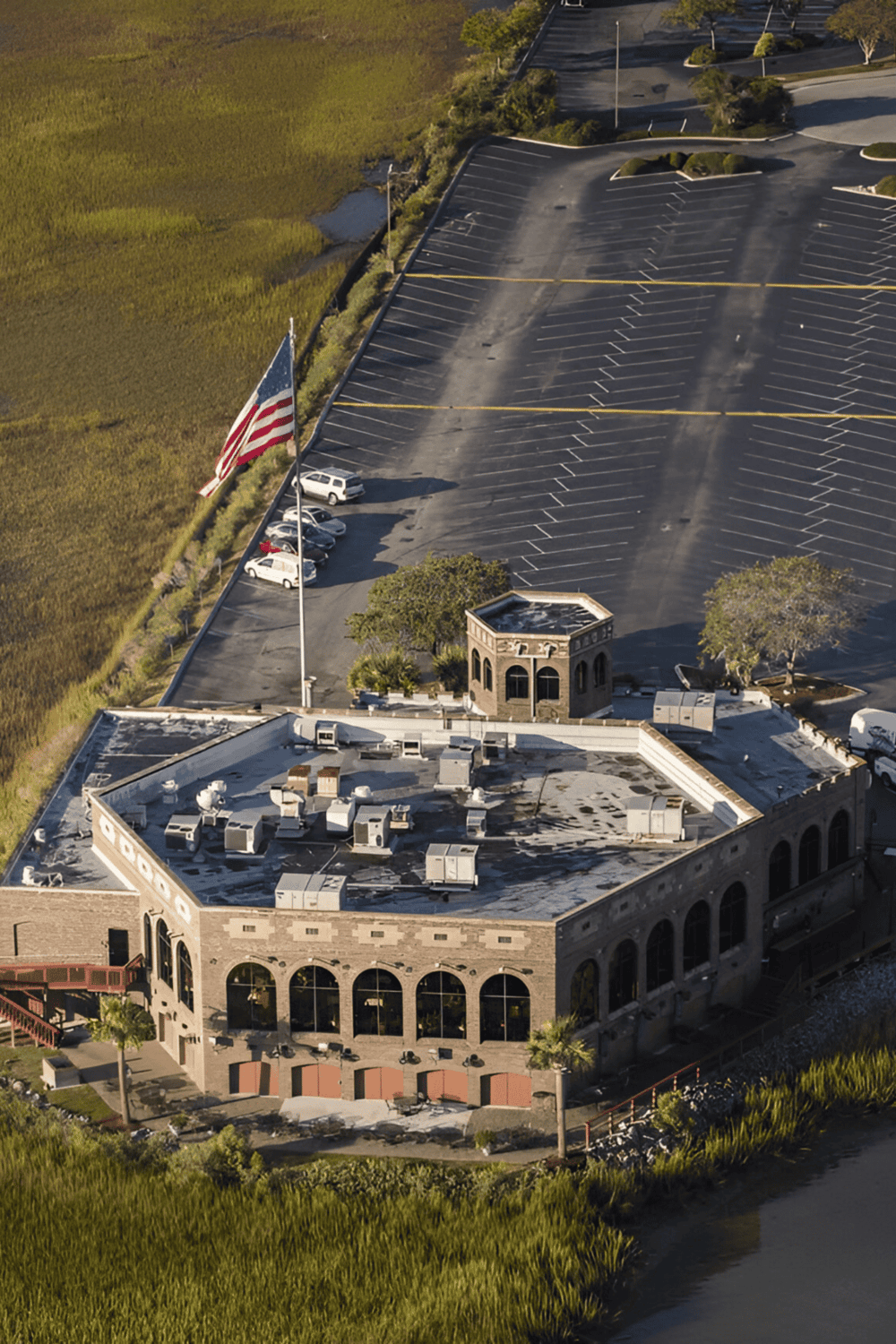 Aerial view of QuestForDirections parking lot with an American flag and a historic building, surrounded by nature.