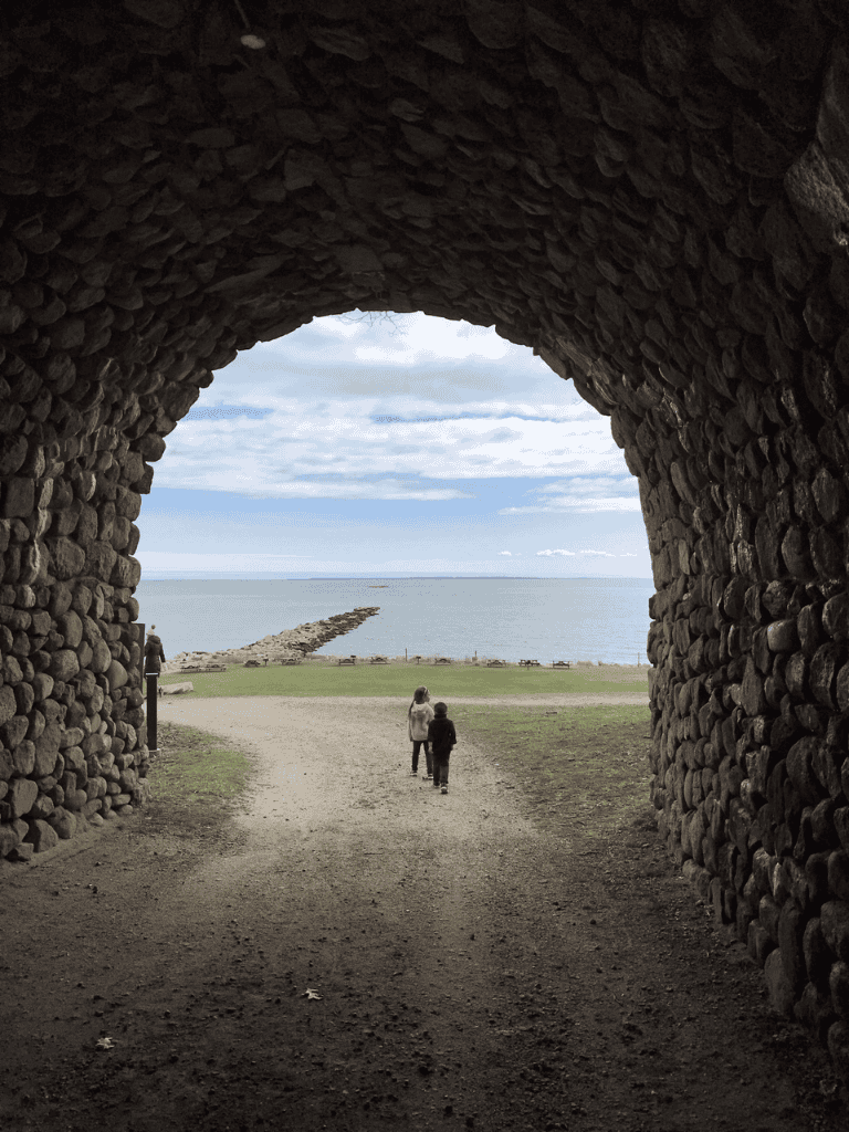 Vast ocean view through stone arch tunnel with walking path and two people by the shore.