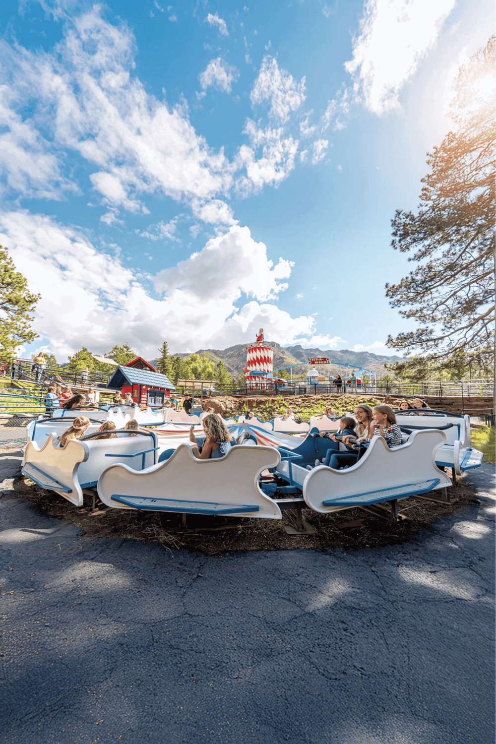 Whimsical amusement park ride with kids enjoying scenic views and mountain backdrop during daytime.