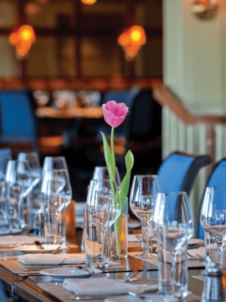 Elegant restaurant table setting with pink tulip centerpiece, glassware, and candle lighting for a romantic dining experience.