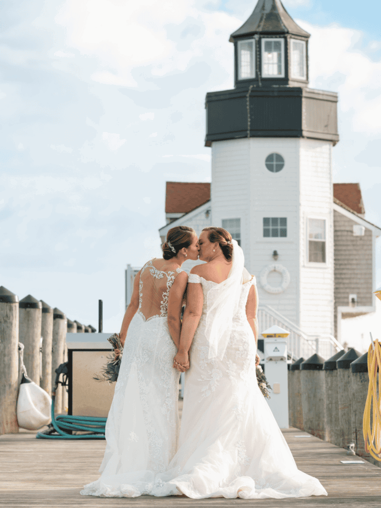 Elegant wedding bride couples kissing by lighthouse on waterfront dock.