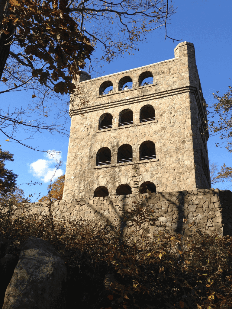 Ancient stone tower with arched windows surrounded by fall foliage, on a clear blue sky day.
