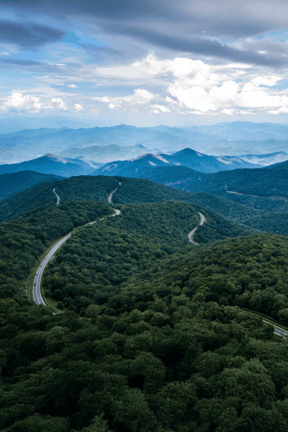 Scenic mountain landscape with winding road and lush green forest in a remote area.