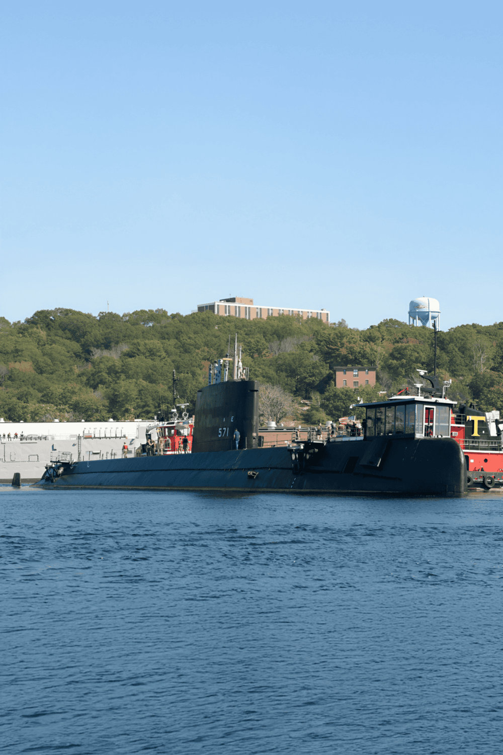 Submarine docked at harbor with scenic green hills in the background, showcasing maritime navigation and waterway transport.