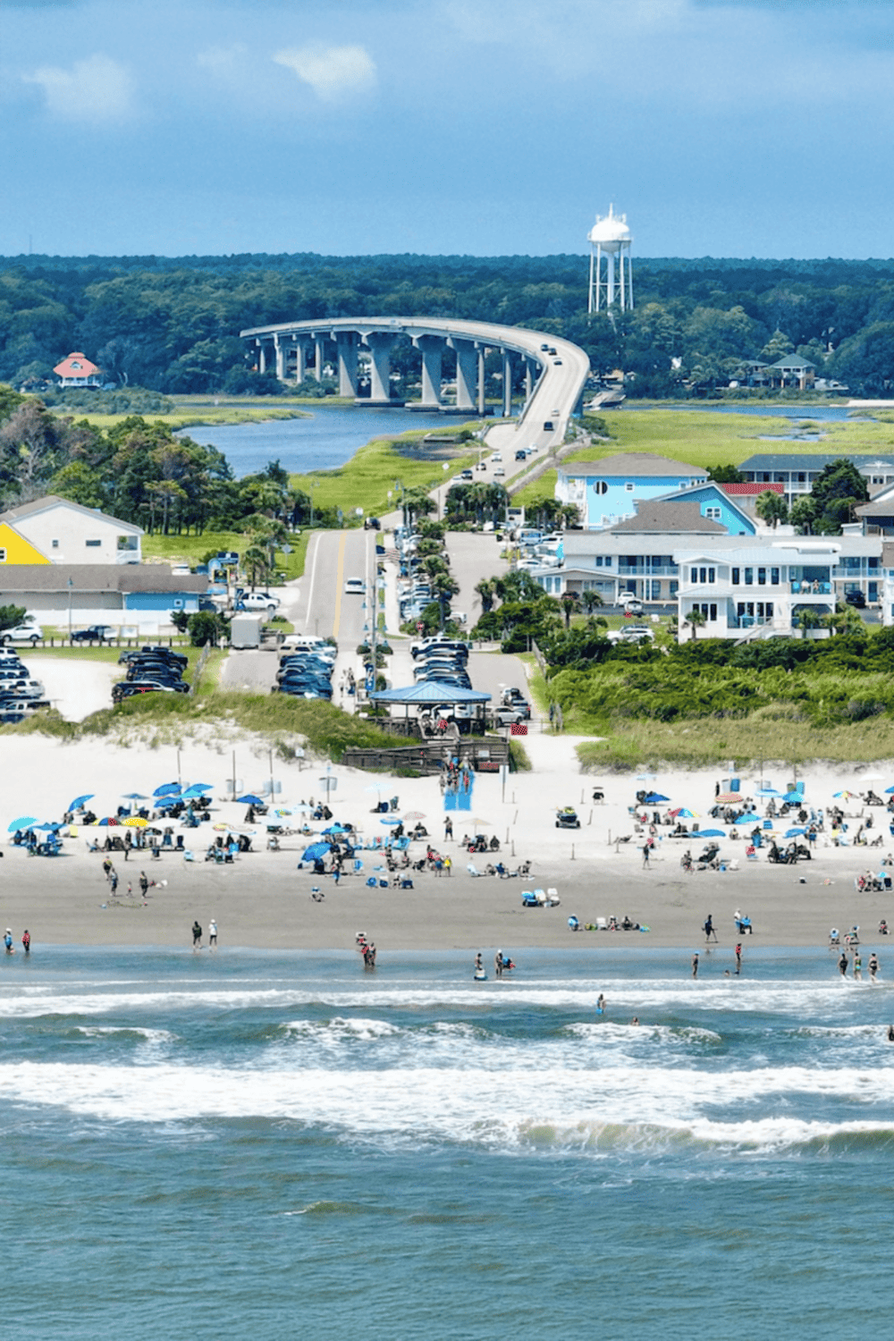 Scenic coastal view with beach, bridge, and water tower in a vibrant coastal town.