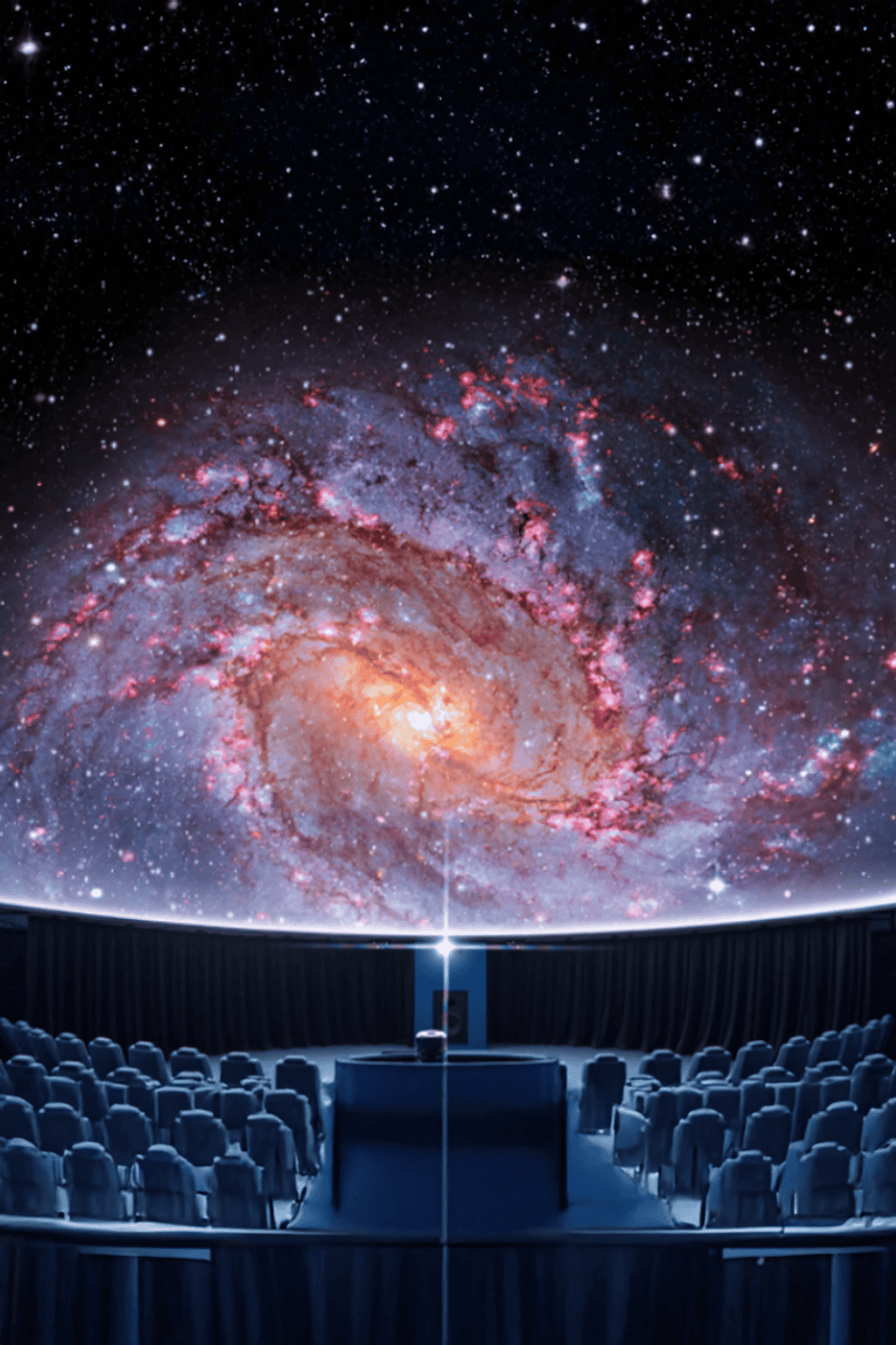 Vast galaxy projection on a large cinema screen in an observatory theater.