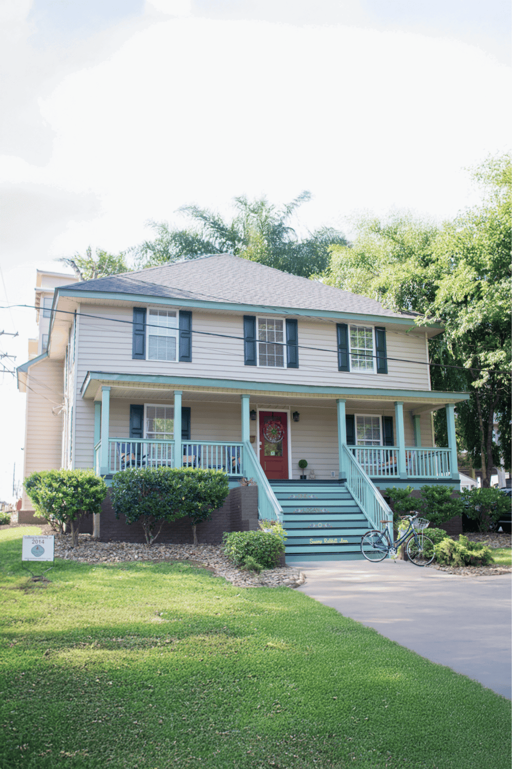 Colorful two-story house with a front porch, well-maintained lawn, and bicycle in a neighborhood setting.