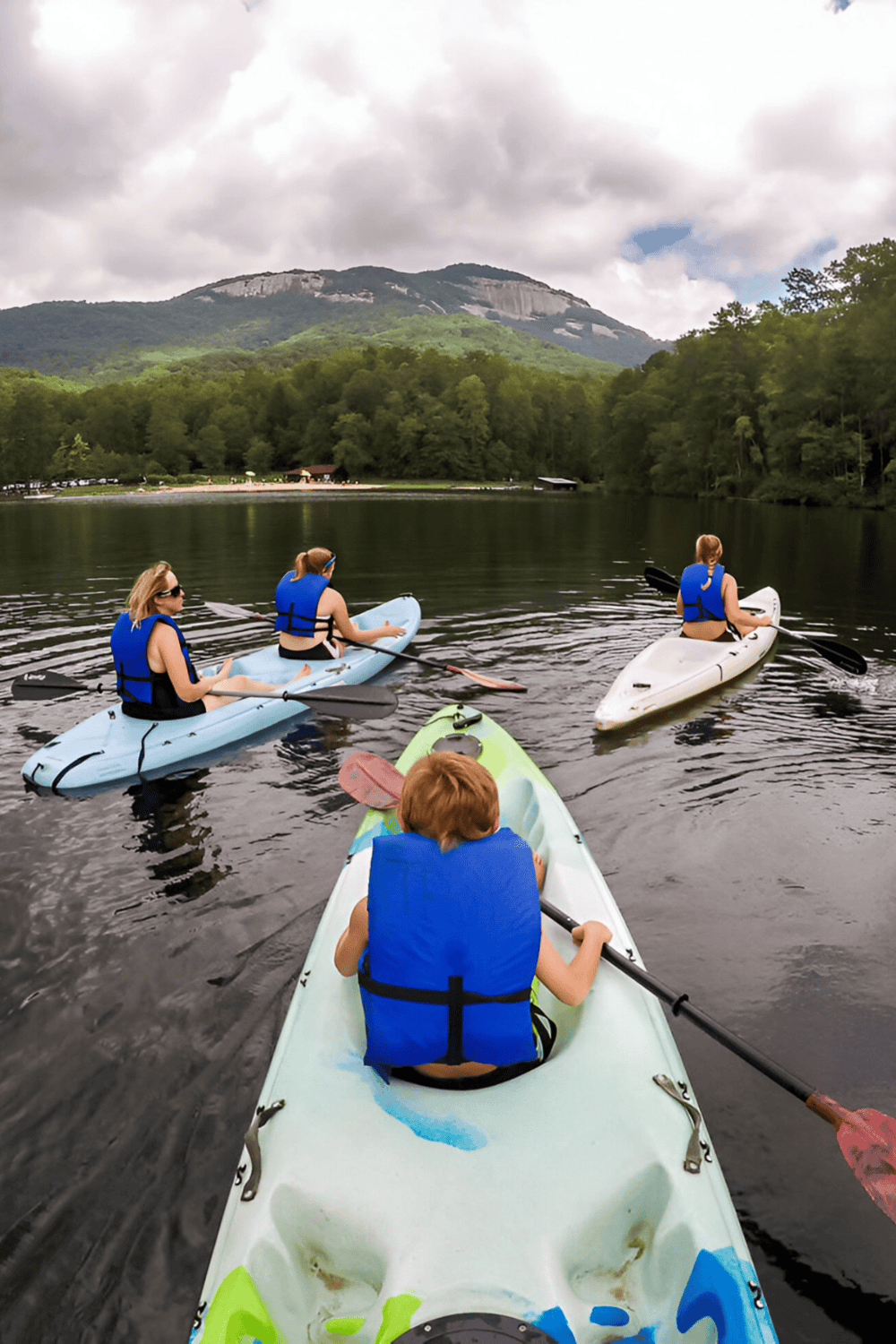 Kids kayaking on a scenic lake with mountain views and lush green trees in the background.