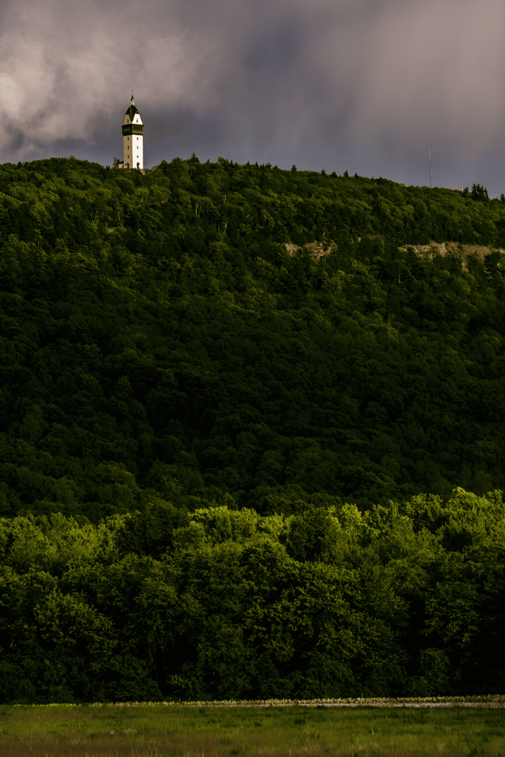 Lighthouse on green hilltop with dark stormy sky, scenic landscape, outdoor navigation, QuestForDirections.