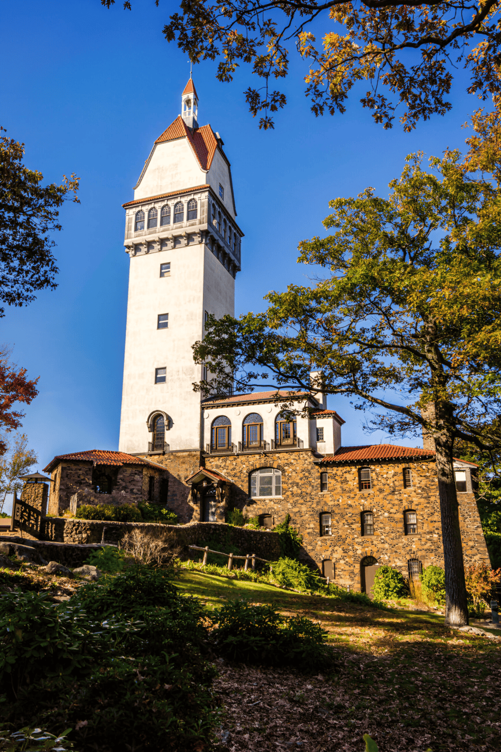 Historic lighthouse tower amidst trees with clear blue sky, featuring QuestForDirections branding, showcasing travel navigation expertise.