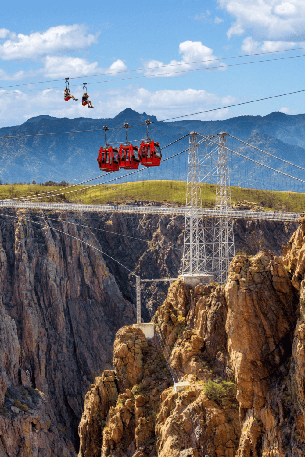 Escalator zip line over rocky canyon with mountain backdrop and blue sky.
