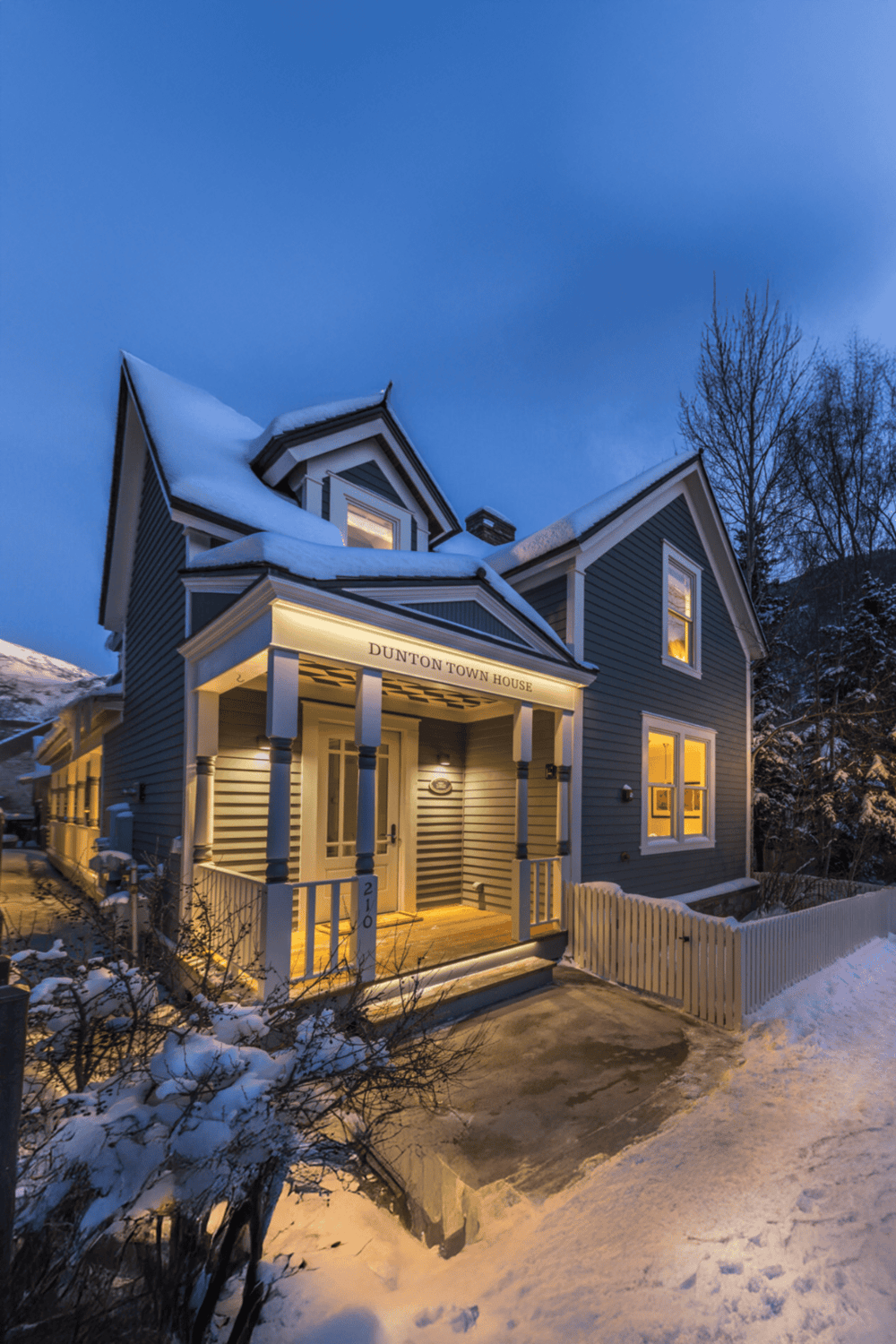 Charming blue Victorian house in winter, illuminated exterior, snowy landscape, Duntontown House, cozy mountain retreat.