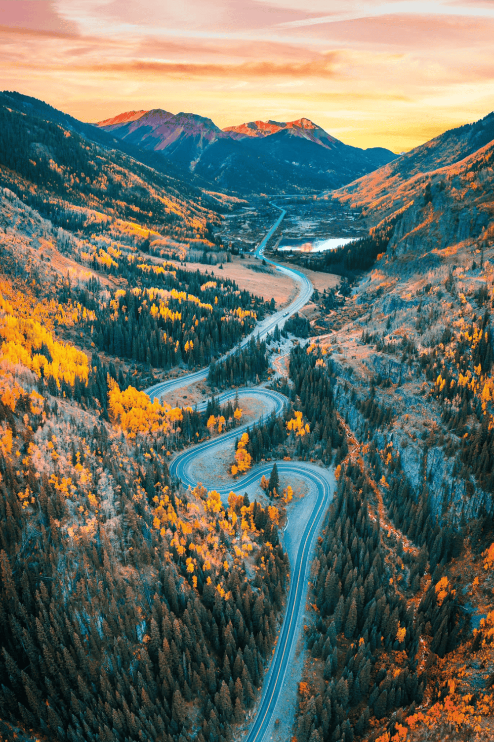 Winding mountain road through colorful autumn forest with mountains in background.