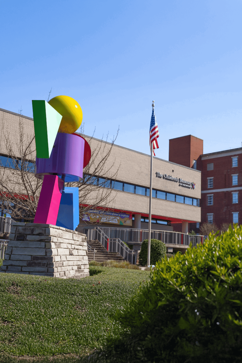 Colorful modern sculpture in front of The Children's Museum of Memphis, with American flag and clear blue sky.