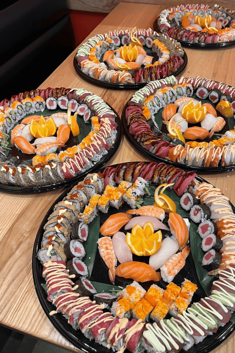 Assorted sushi platters with variety of rolls, sashimi, and garnishes on a wooden table.