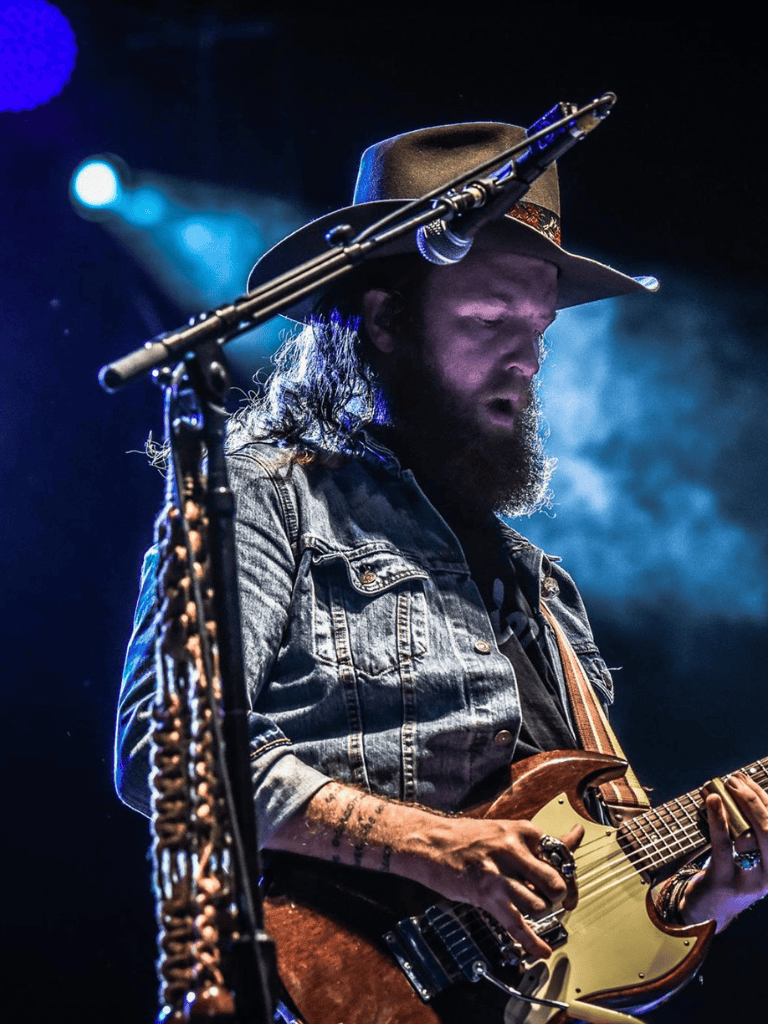 Vintage musician playing electric guitar on stage with blue lighting and smoke effects, live music performance.