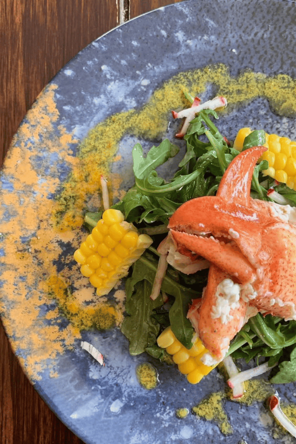 Fresh lobster salad with corn and mixed greens on artistic blue plate, perfect for seafood fans and gourmet dining.