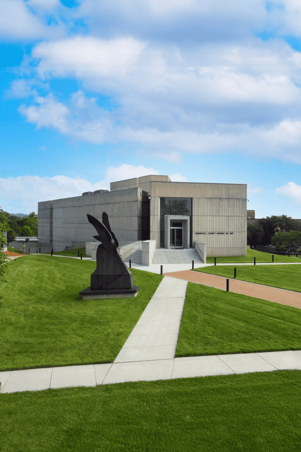 Modern courthouse building with sculpture, scenic lawn, and clear sky.