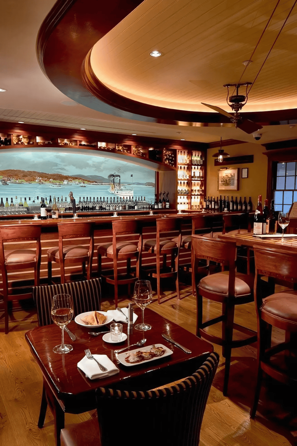 Cozy waterfront restaurant interior with wine bottles and ocean view, perfect for dining and wine tasting.
