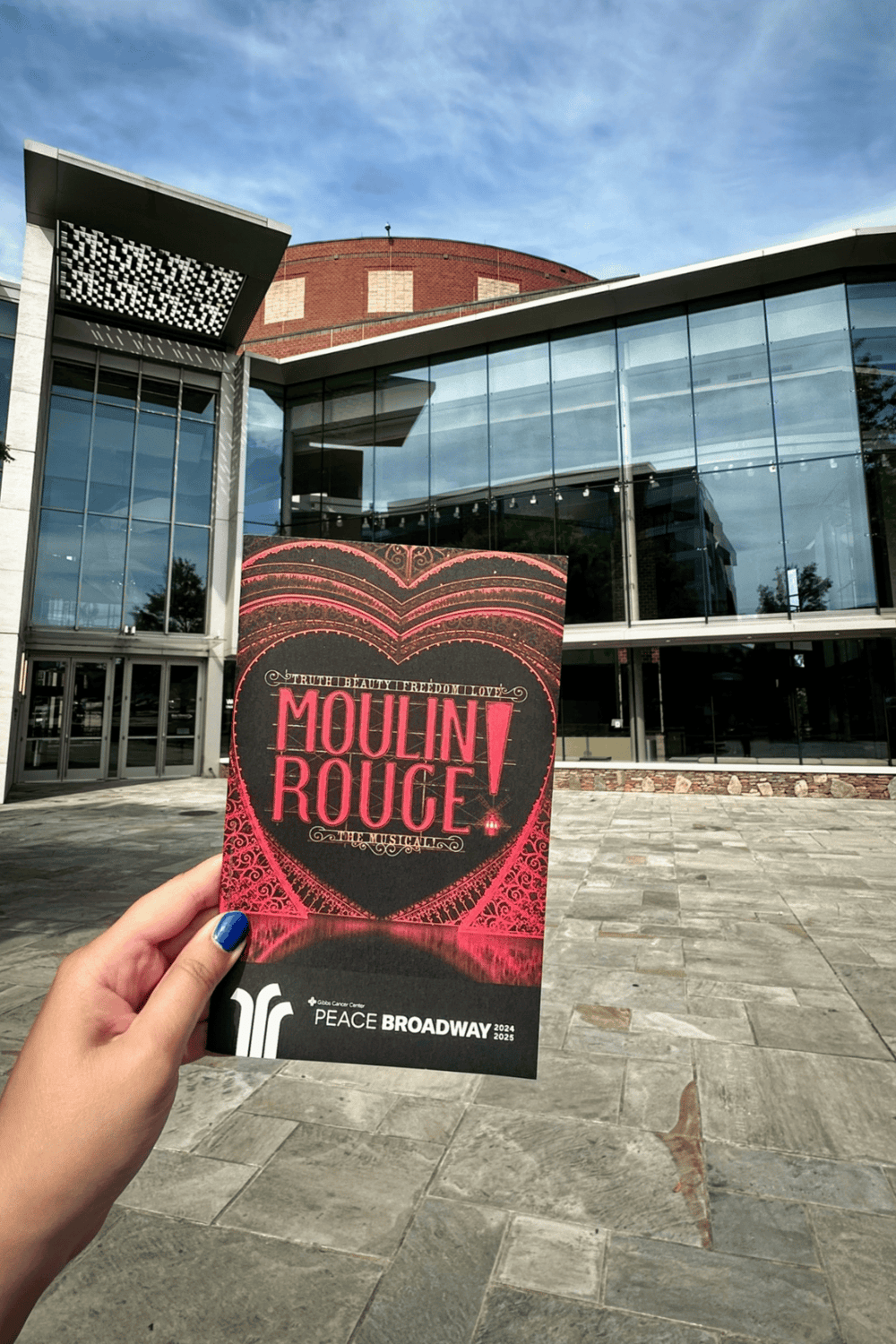 Moulin Rouge! Broadway theater ticket in front of modern building, promoting entertainment venue and cultural events.