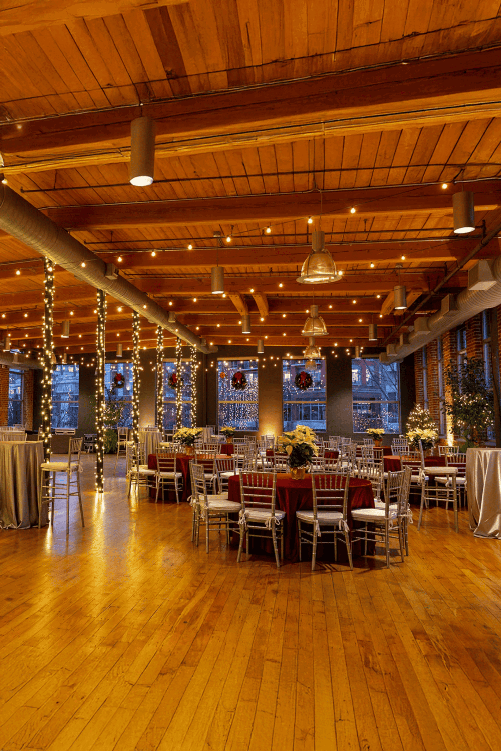 Cozy holiday-themed event space with string lights, decorated tables, and festive wreaths, perfect for celebrations.
