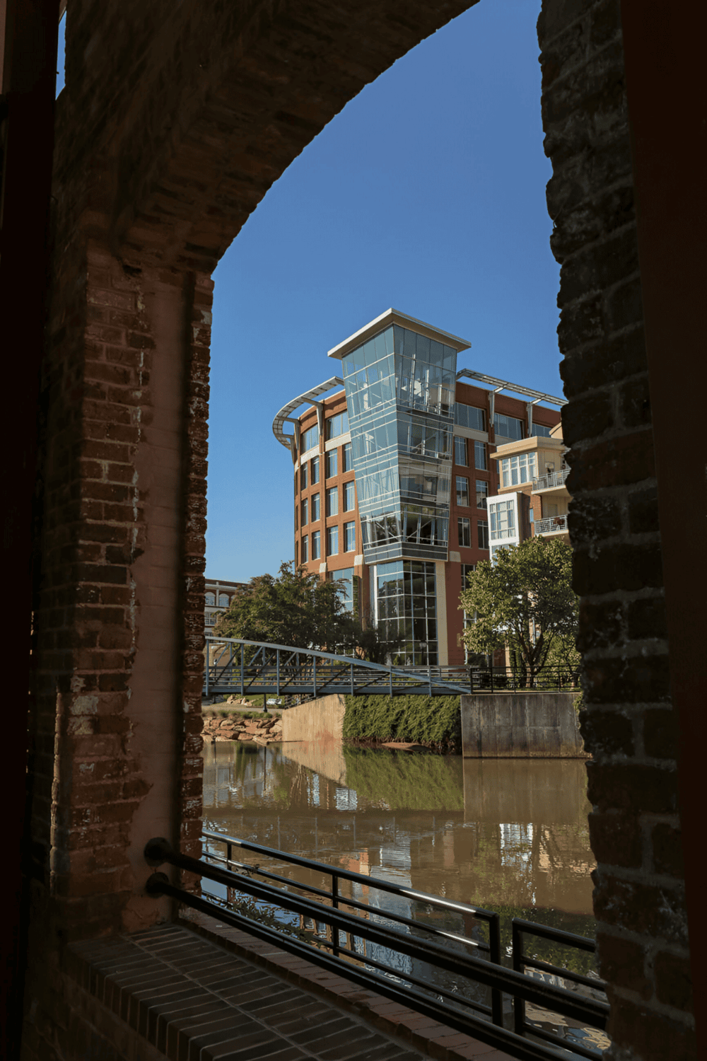 Modern city building with glass facade through historical brick archway.