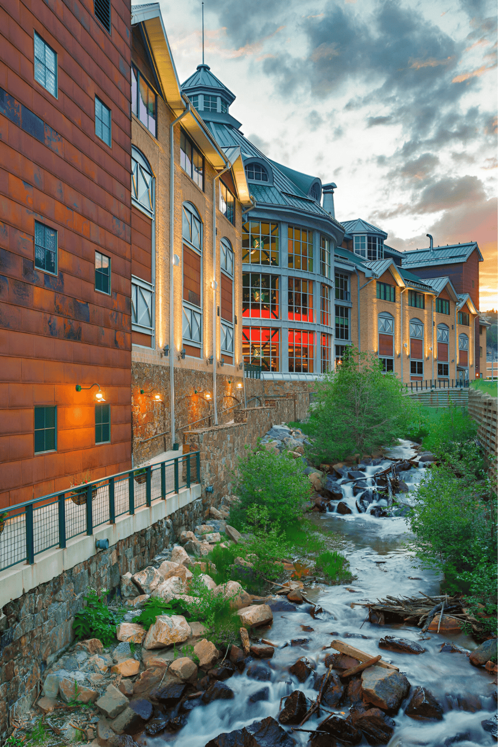 Charming hotel by a flowing creek with scenic mountain views at sunset, emphasizing travel and accommodation near nature.