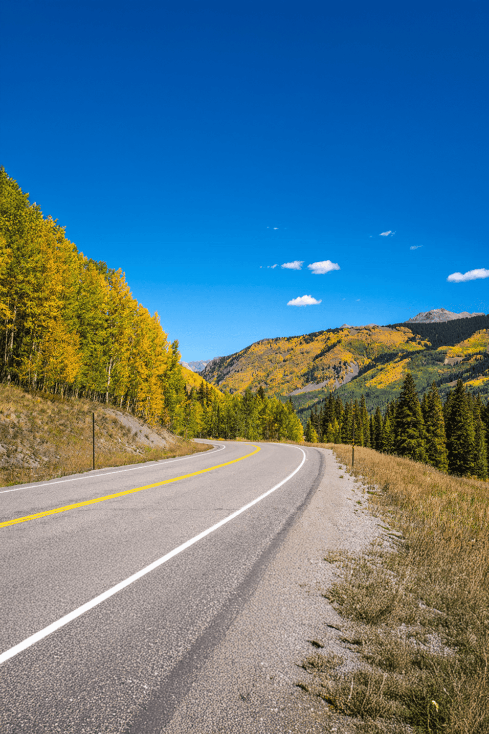 Winding mountain road through fall foliage under clear blue sky, scenic outdoor travel route in nature.