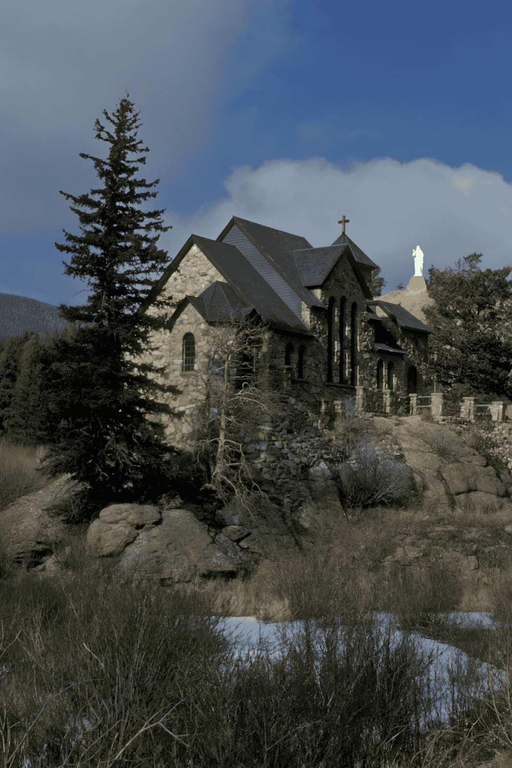 Historic church building located in a scenic mountain landscape with trees and a cross on the roof.