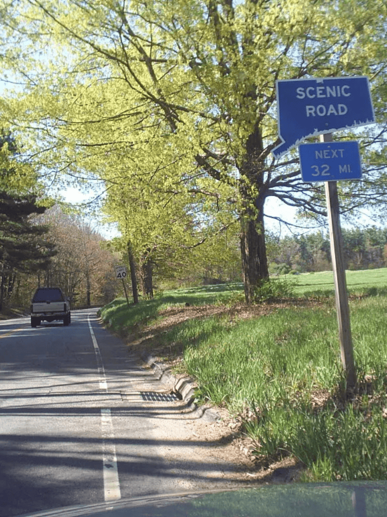 Scenic road sign on green roadside with trees, indicating next 32 miles, perfect for travel and navigation.