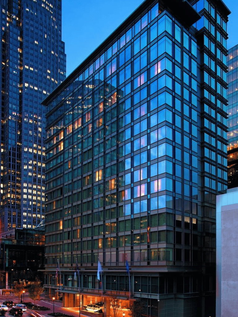 Modern glass office building in city skyline during evening, illuminated windows and vibrant reflections.