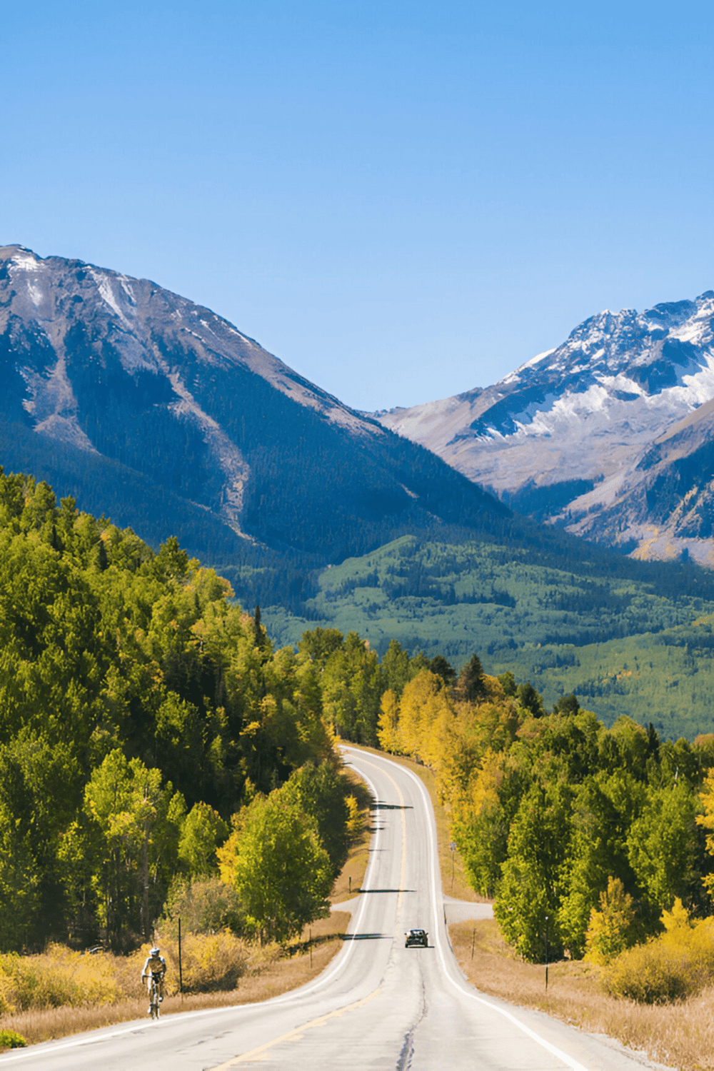 Idyllic mountain road with vibrant fall foliage and snow-capped peaks in the background.