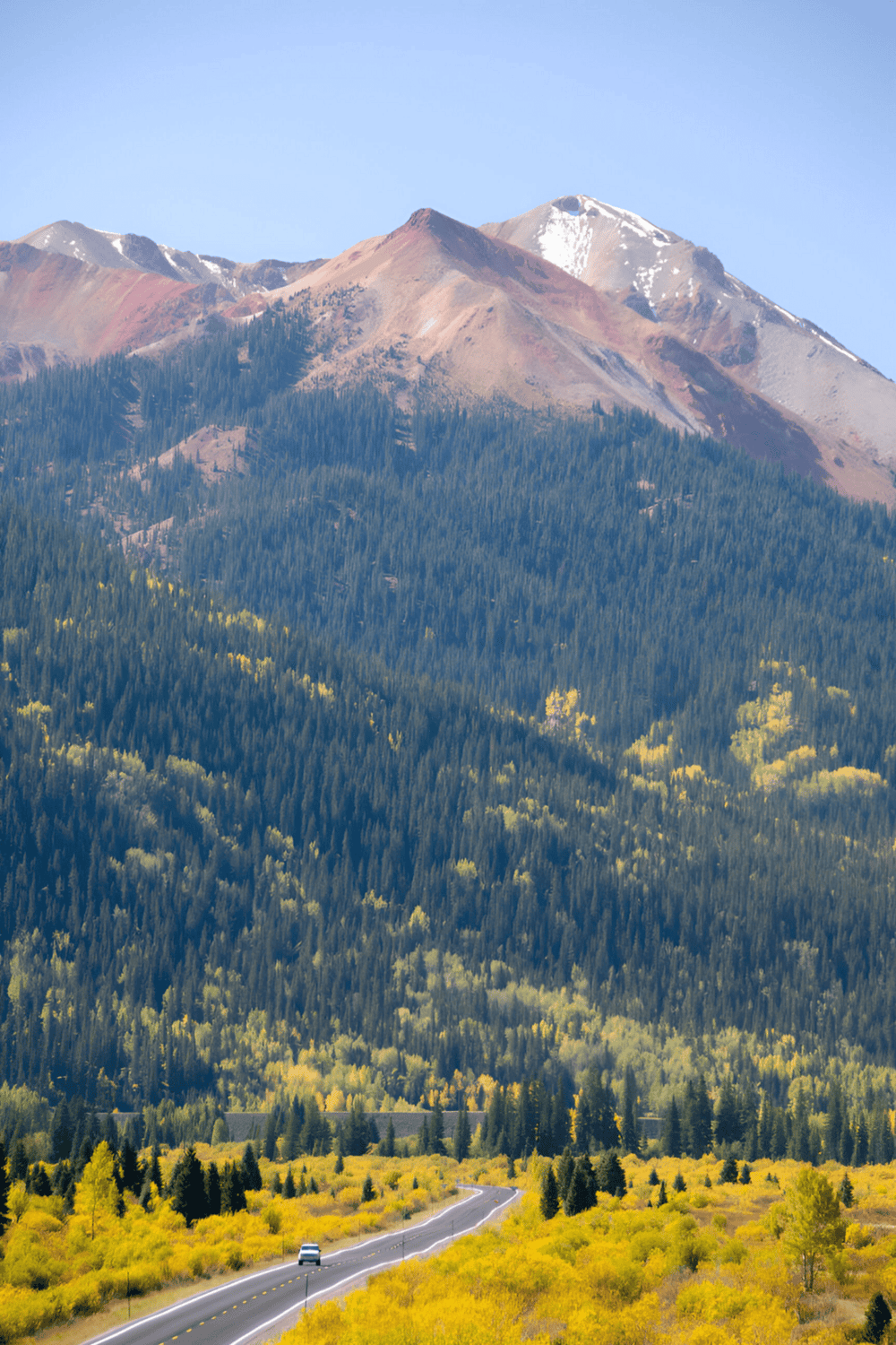 Vibrant mountain landscape with winding road, colorful trees, and snow-capped peaks, showcasing scenic outdoor adventure destinations.