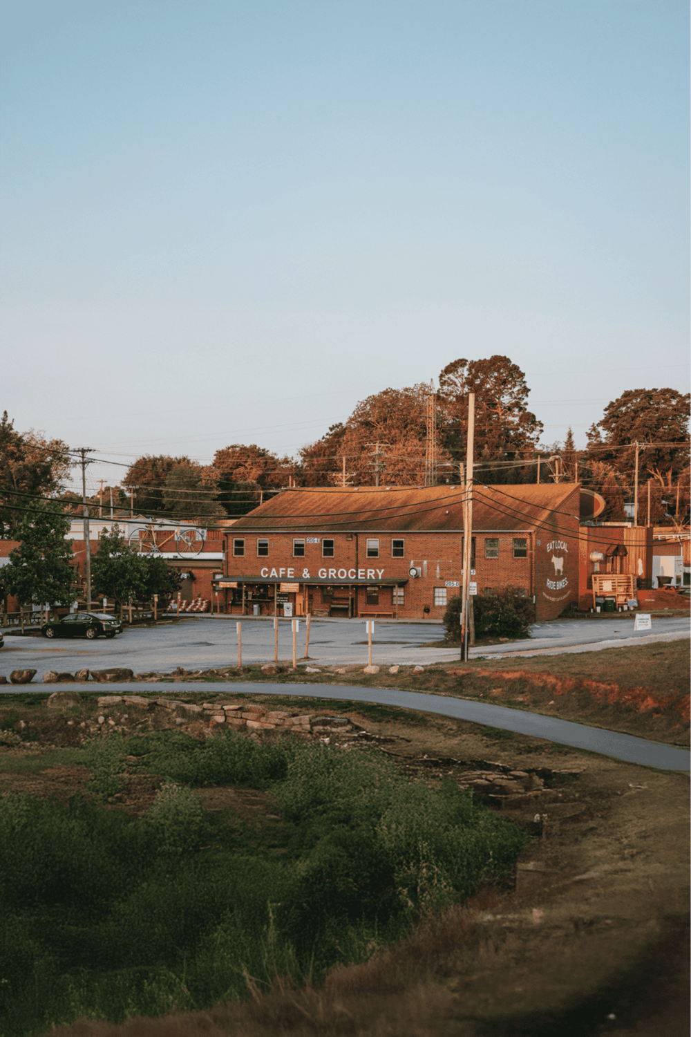 Historic brick cafe and grocery store in small town with parking lot and trees at sunset.