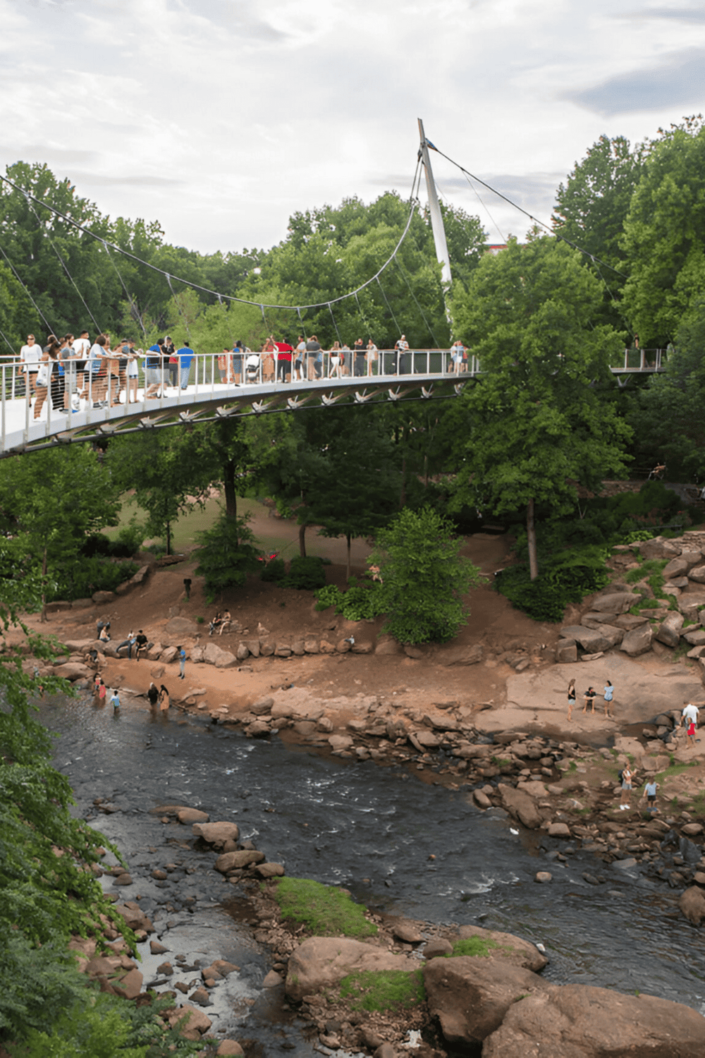 People walking on the Canopy Walk at Quest for Directions park, surrounded by lush greenery.