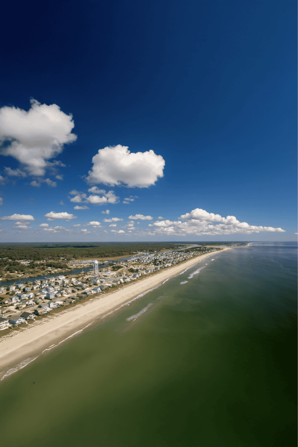 Seaside coastal town with beach, residential area, and clear blue sky, ideal for travel and navigation.