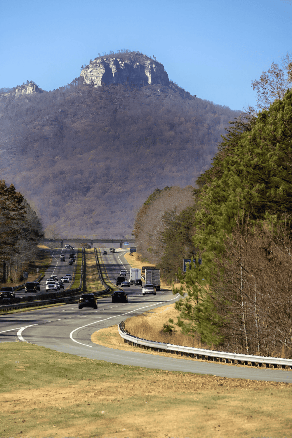 Scenic mountain highway view with lush greenery and distant mountain peak, ideal for travel and navigation.