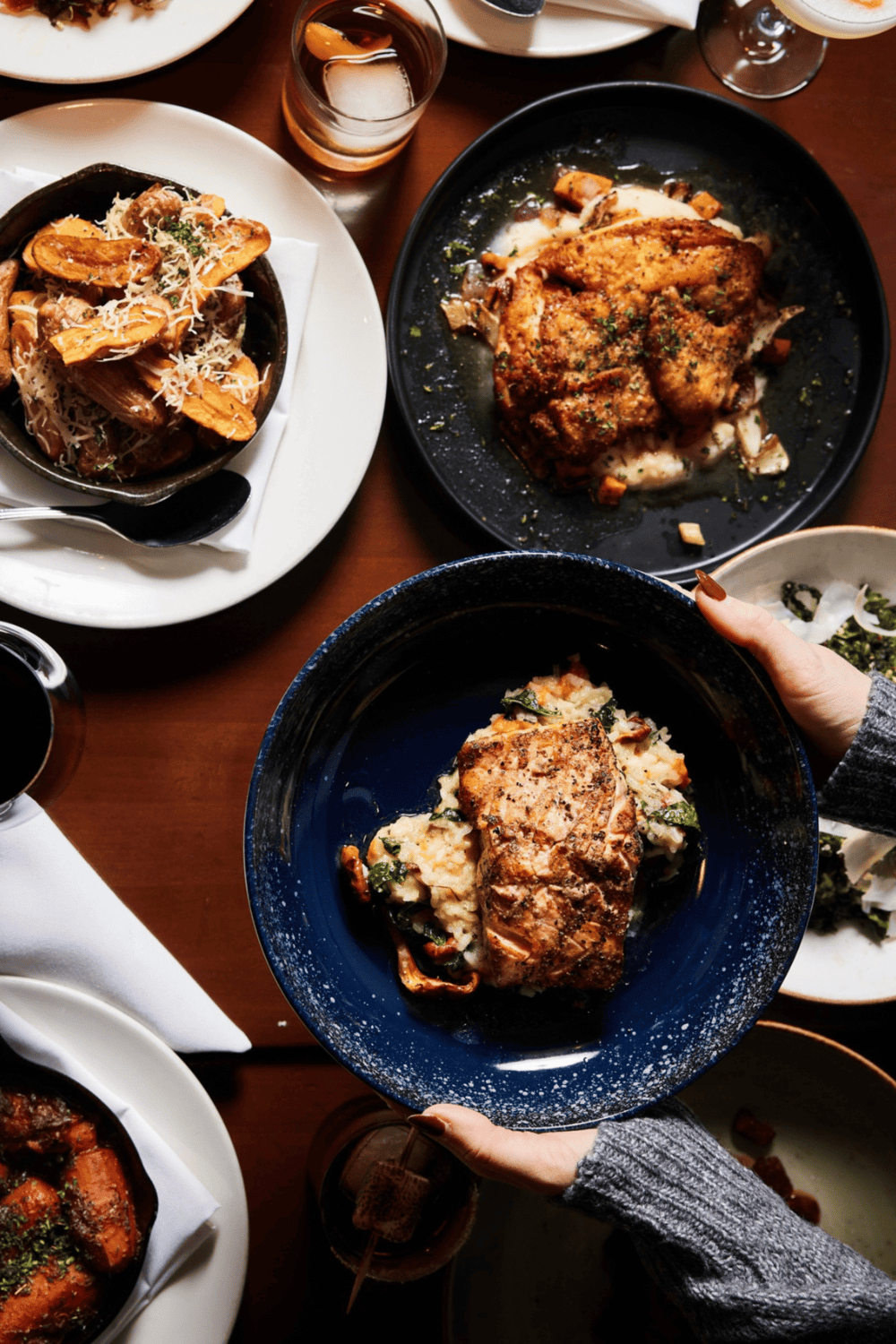 Steak and seafood dishes on a dining table with drinks, showcasing American cuisine.