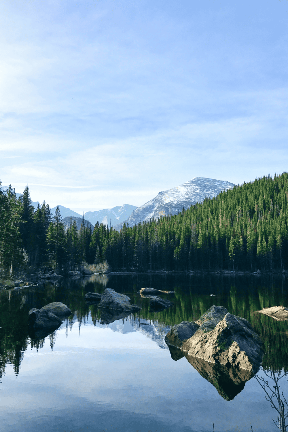 Serene mountain lake with evergreen forest and snow-capped peaks in the background.