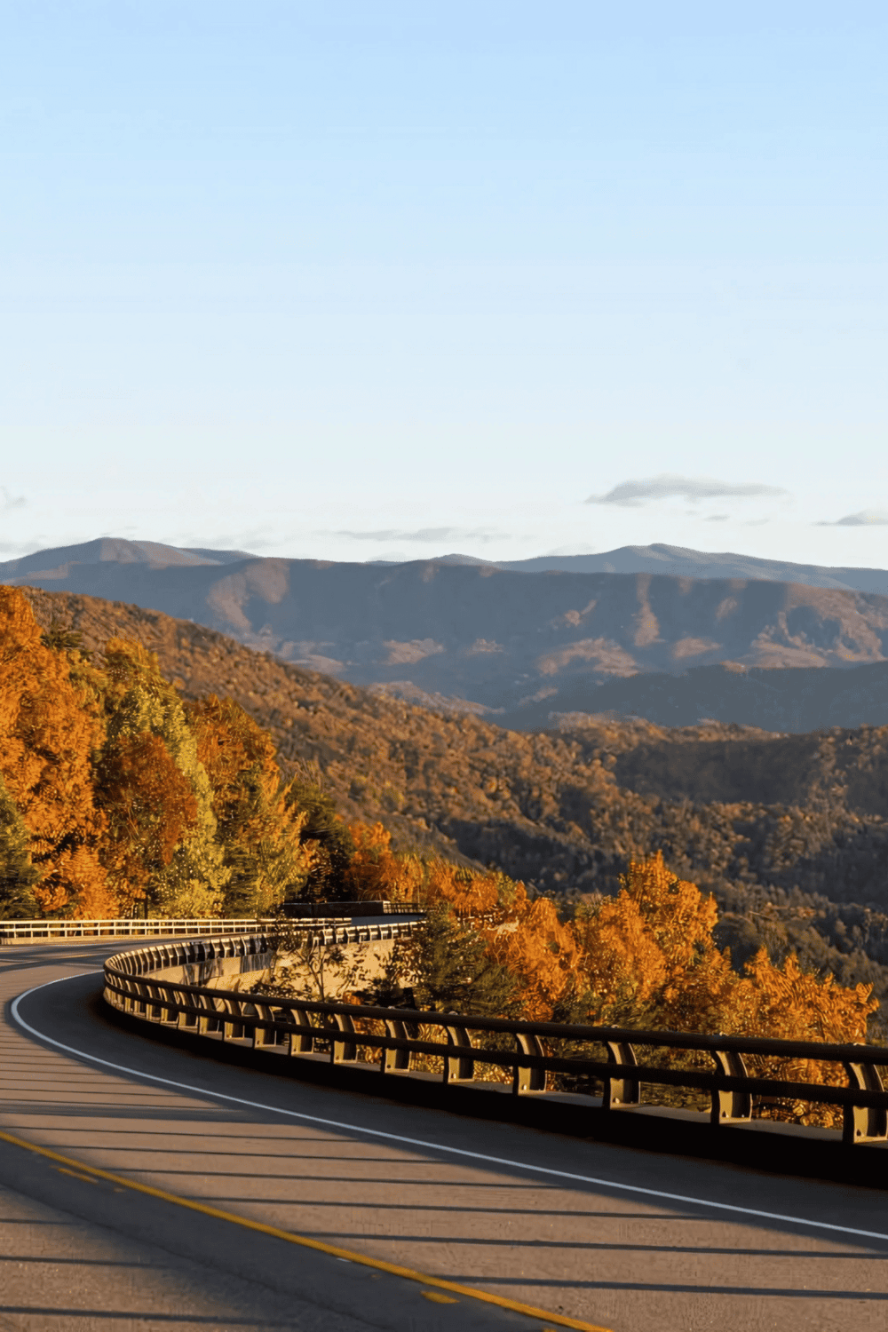 Vivid autumn foliage along a winding mountain road during daytime.