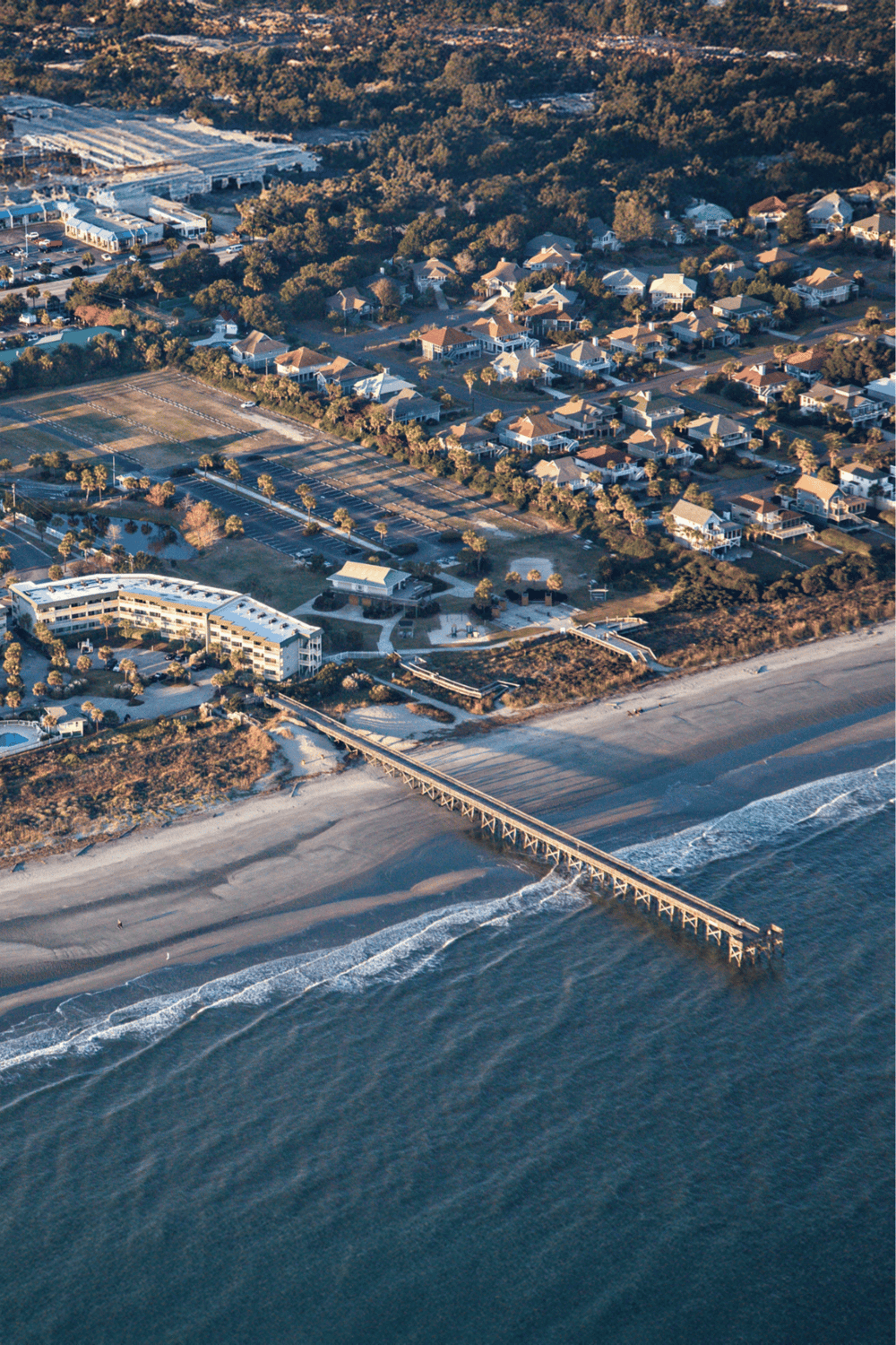 Aerial view of coastal town with houses, beach, and pier.