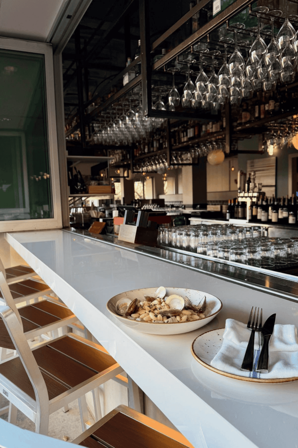 Fresh seafood dish served at a stylish restaurant bar with wine glasses hanging overhead.