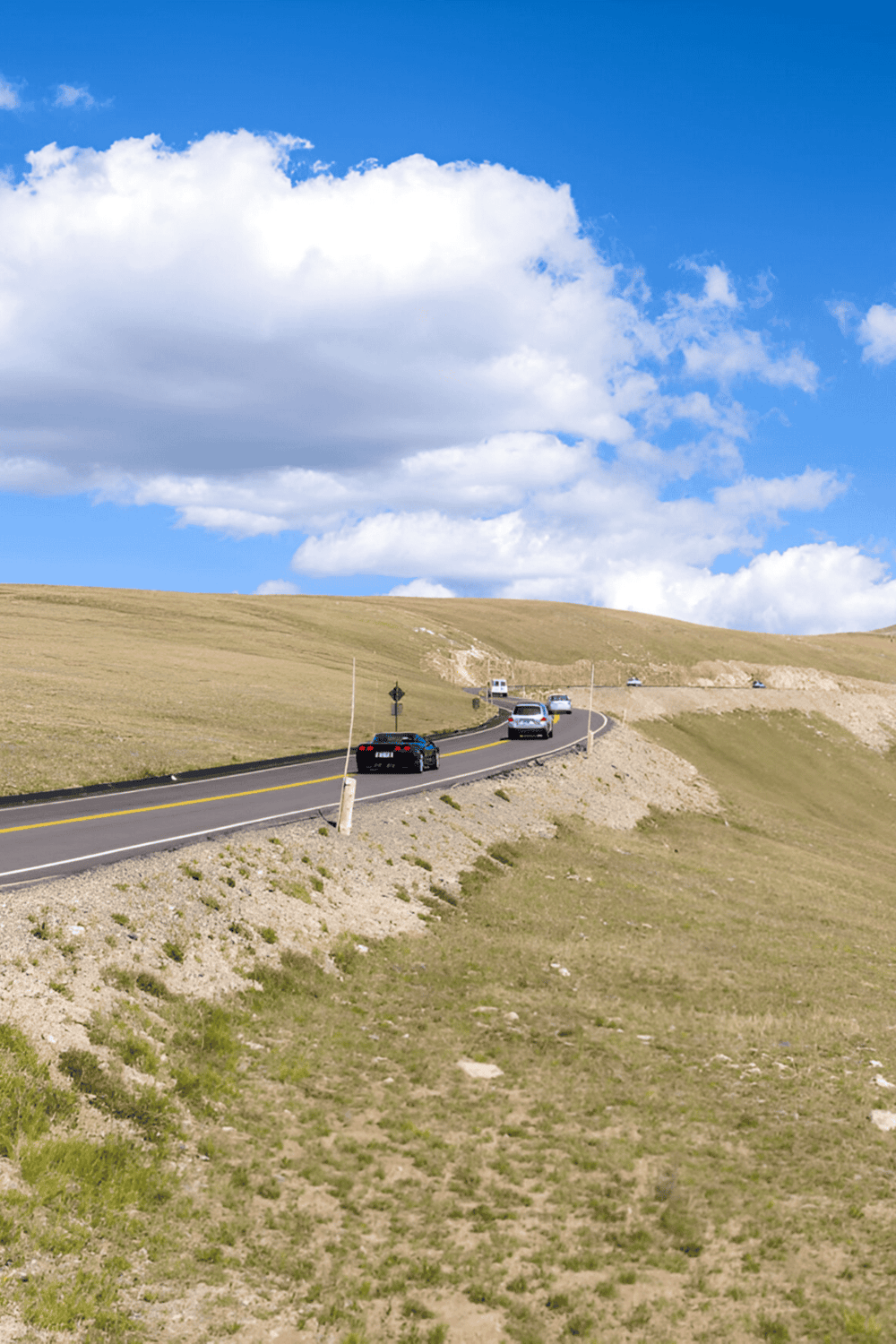 Rolling hills and winding road with traffic, scenic landscape, outdoors, travel, road trip, sunshine, blue sky, nature.