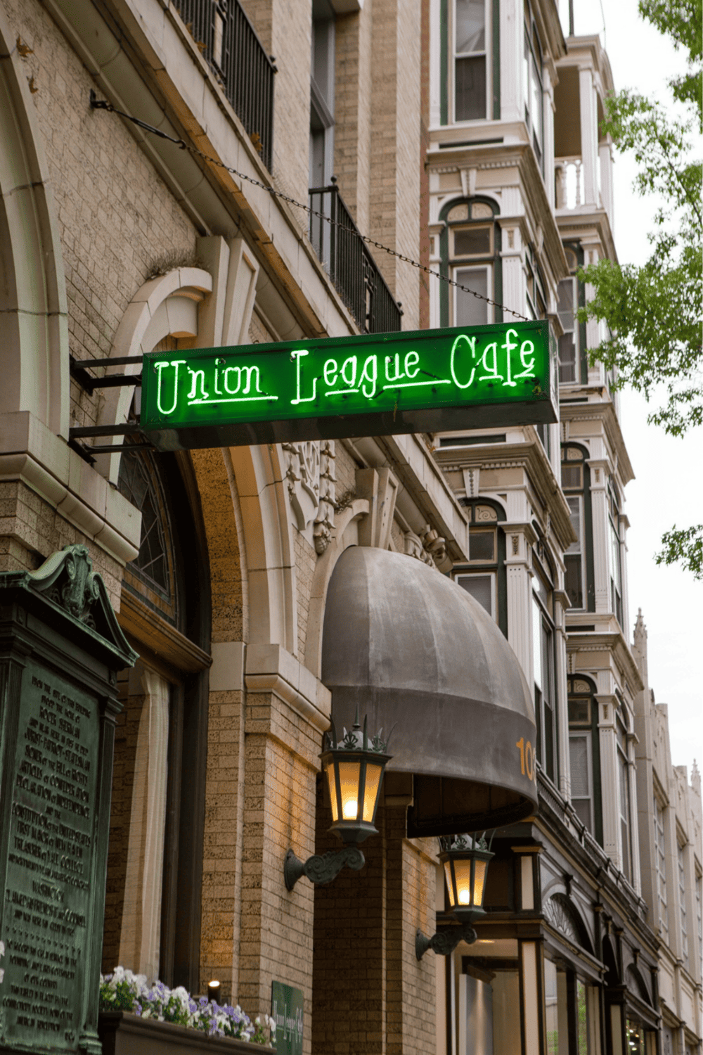 Green neon sign of Union League Cafe in city street setting.