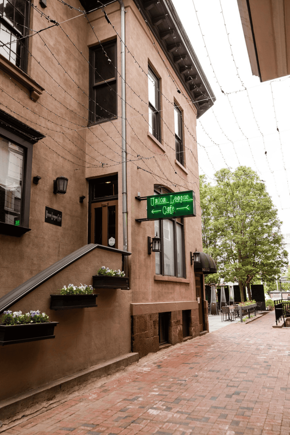 Cozy café exterior with string lights and green neon sign, located on a charming brick sidewalk.