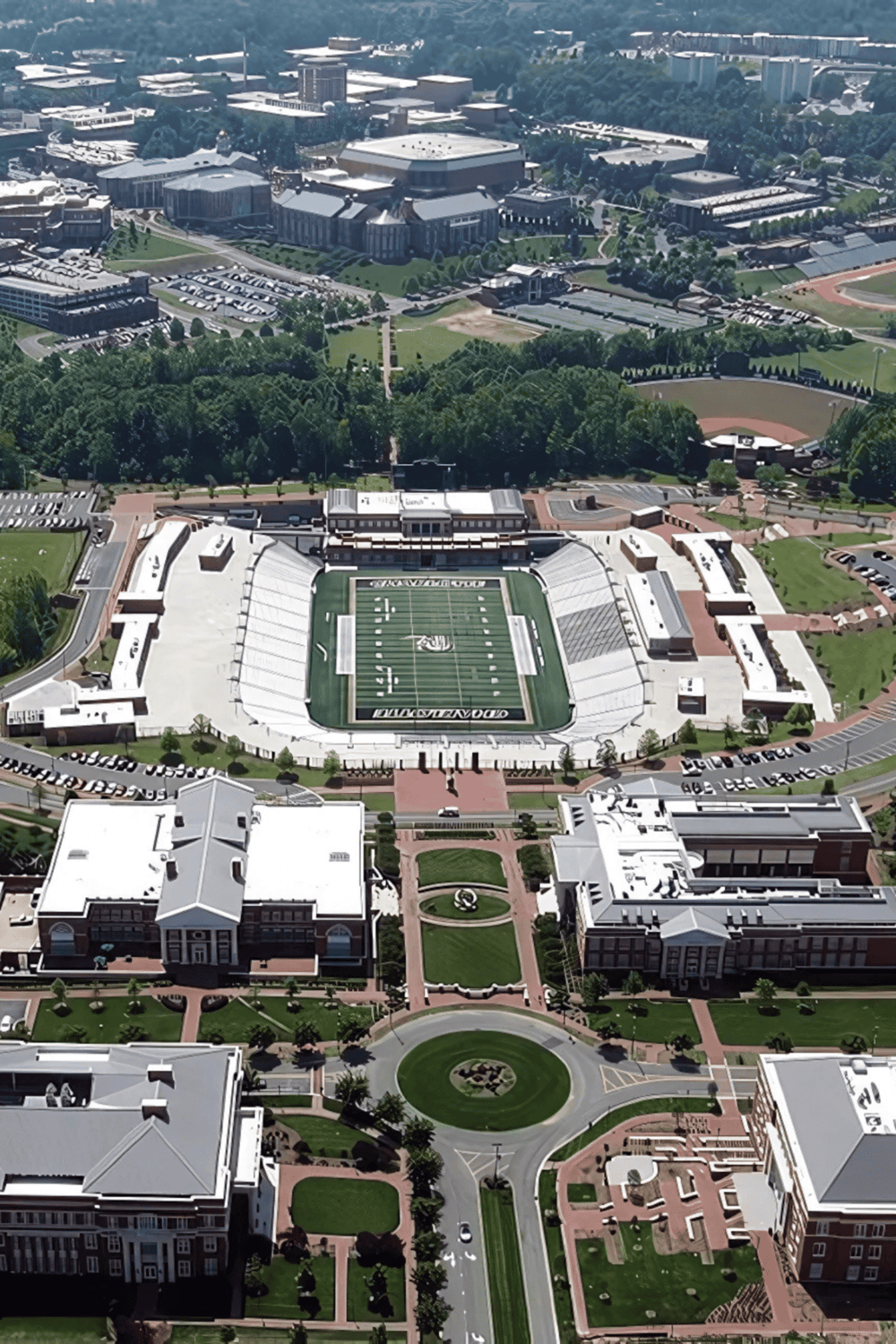 Aerial view of a university campus with football stadium, greenery, and academic buildings.