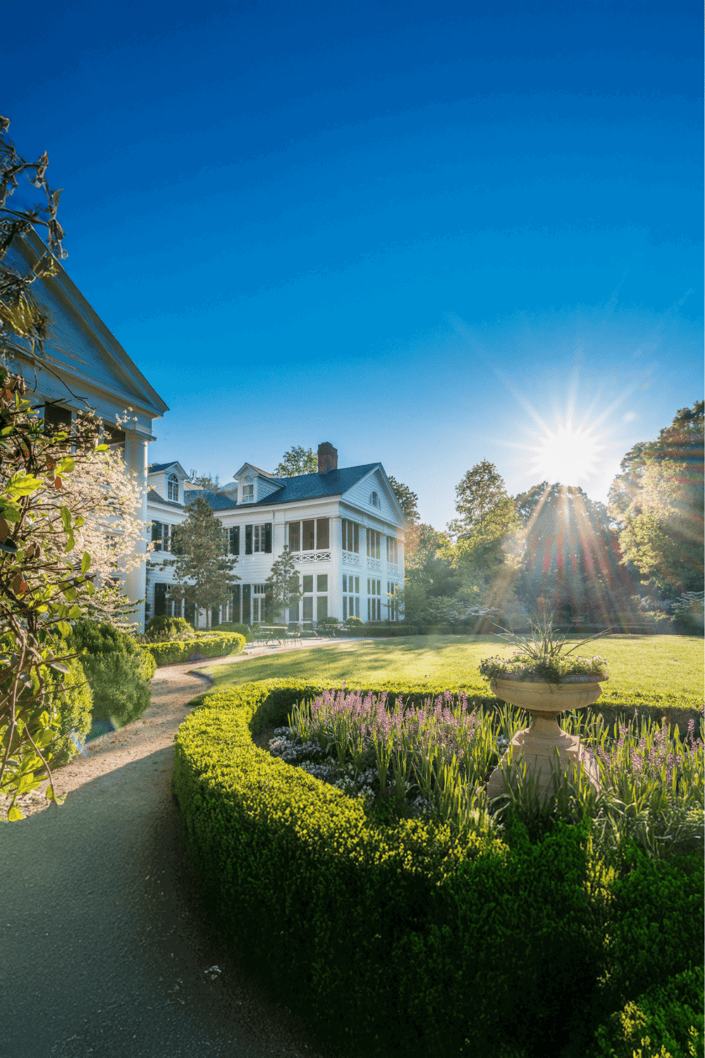 Luxurious mansion with beautiful gardens and vibrant landscaping at sunset.