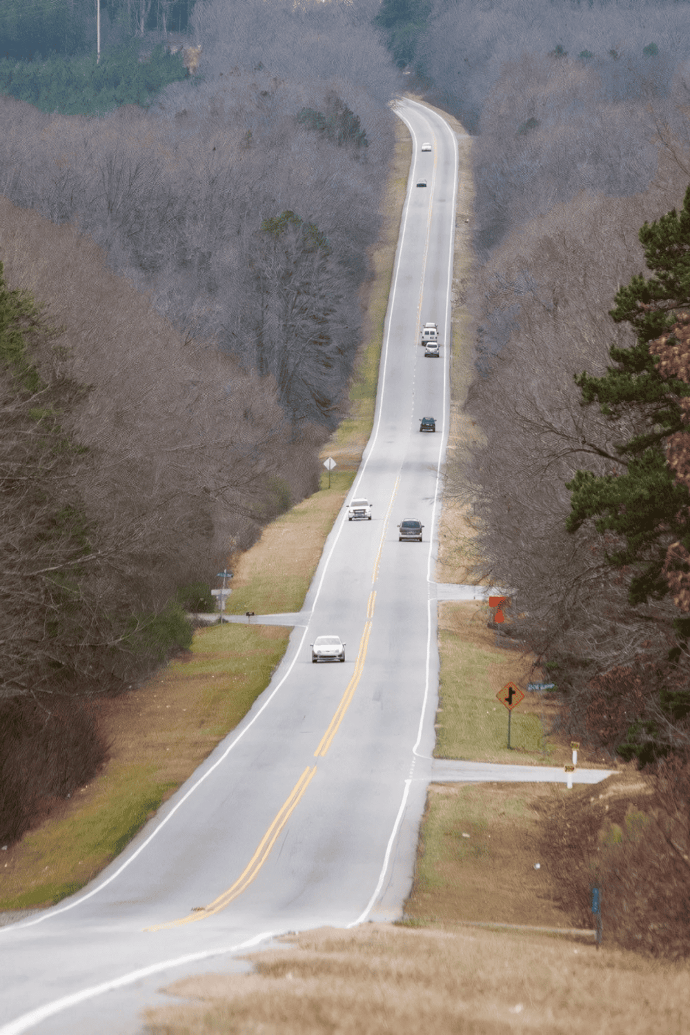 Scenic rural road with cars traveling through a wooded landscape, perfect for navigation and travel planning.