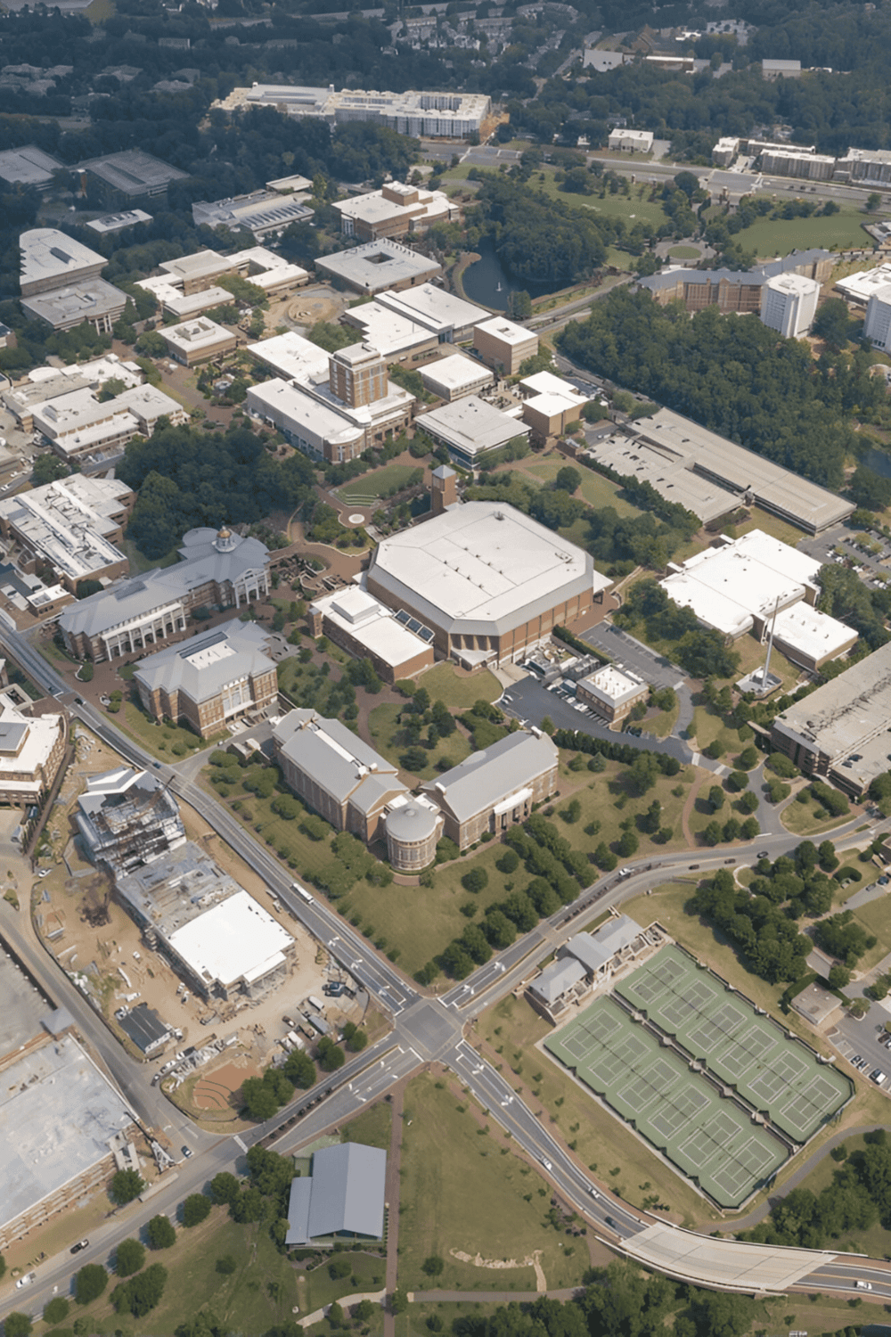 Modern university campus with academic buildings, green spaces, and tennis courts in aerial view.